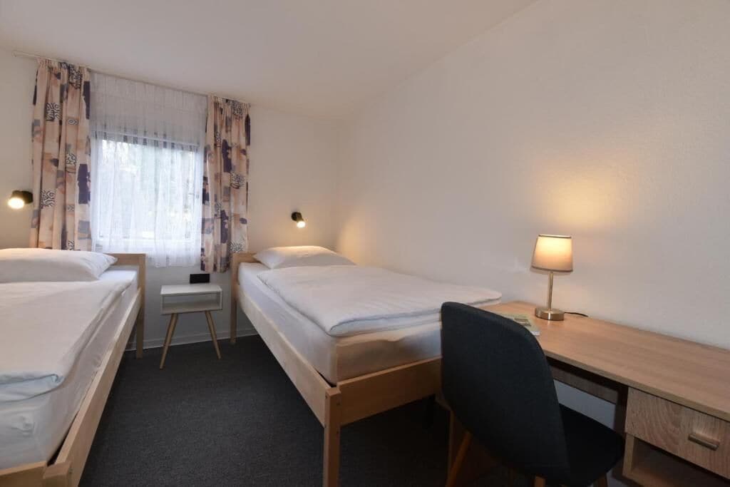 Een hotelkamer met twee eenpersoonsbedden, een bureau met stoel, een lamp en een klein nachtkastje.