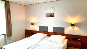 Ein Hotelzimmer mit zwei Einzelbetten, einem Kopfteil mit integriertem Regal, einem Deckenventilator und zwei an der Wand befestigten Nachttischen mit Lampen.