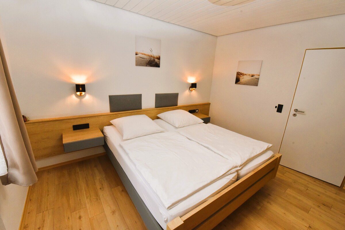 A hotel room with a large bed, two bedside tables, and two wall-mounted lamps.