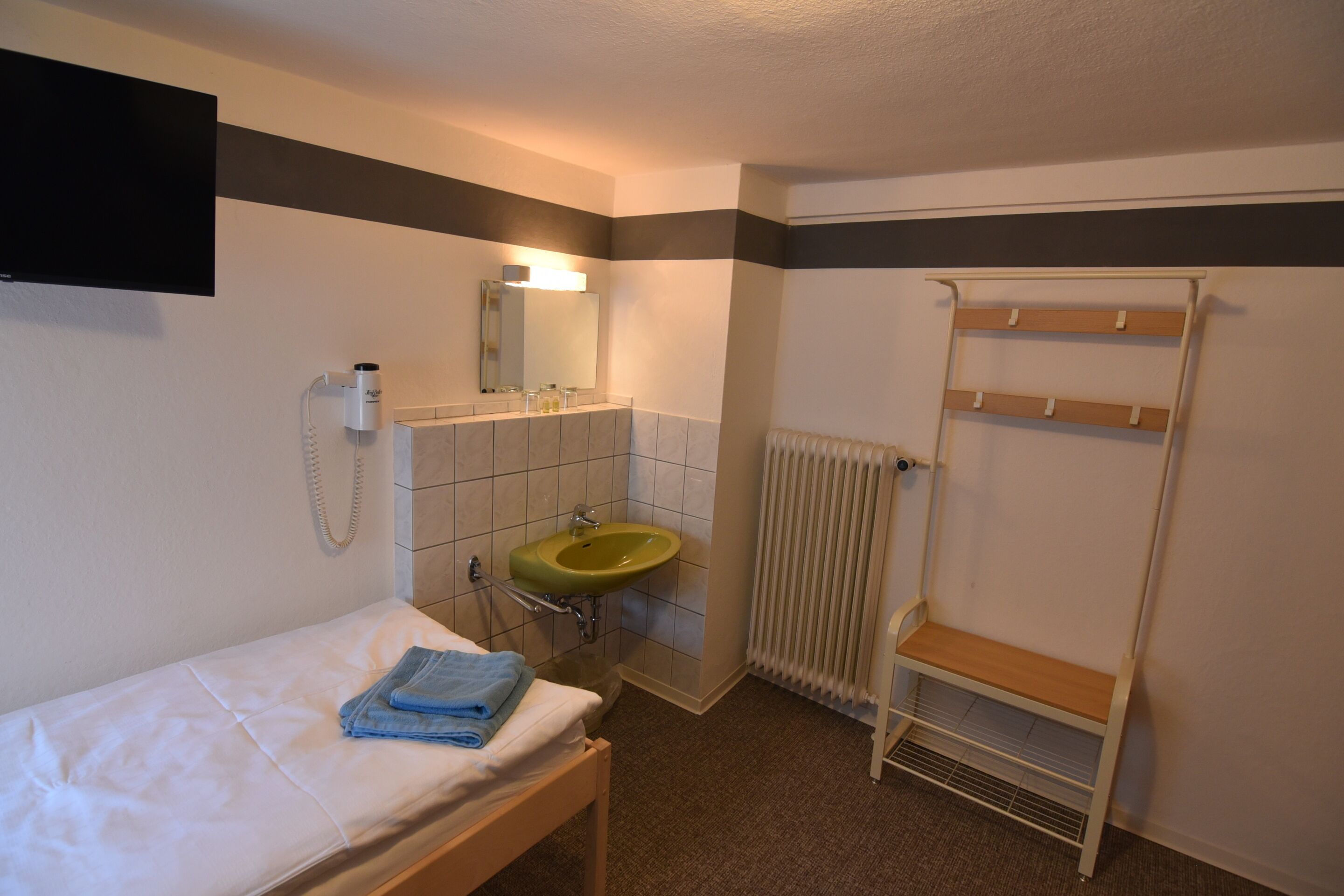 A small, clean room with a bed, a sink, a mirror, and a towel rack.