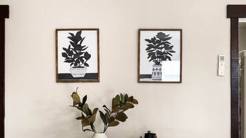 A dining area with a table set for two, a vase with green leaves, and two framed black and white plant illustrations on the wall.