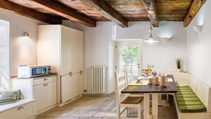 A kitchen with white cabinets, a microwave, a table with chairs, a radiator, and a window with a view of greenery. - VILLAROSA SPICCIANO Exclusive Villa with pool (Fivizzano/Spicciano)
