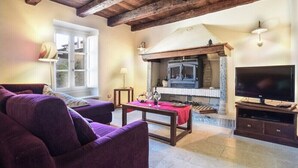 A living room with a fireplace, a sofa, a television, and a table with a red cloth. - VILLAROSA SPICCIANO Exclusive Villa with pool (Fivizzano/Spicciano)