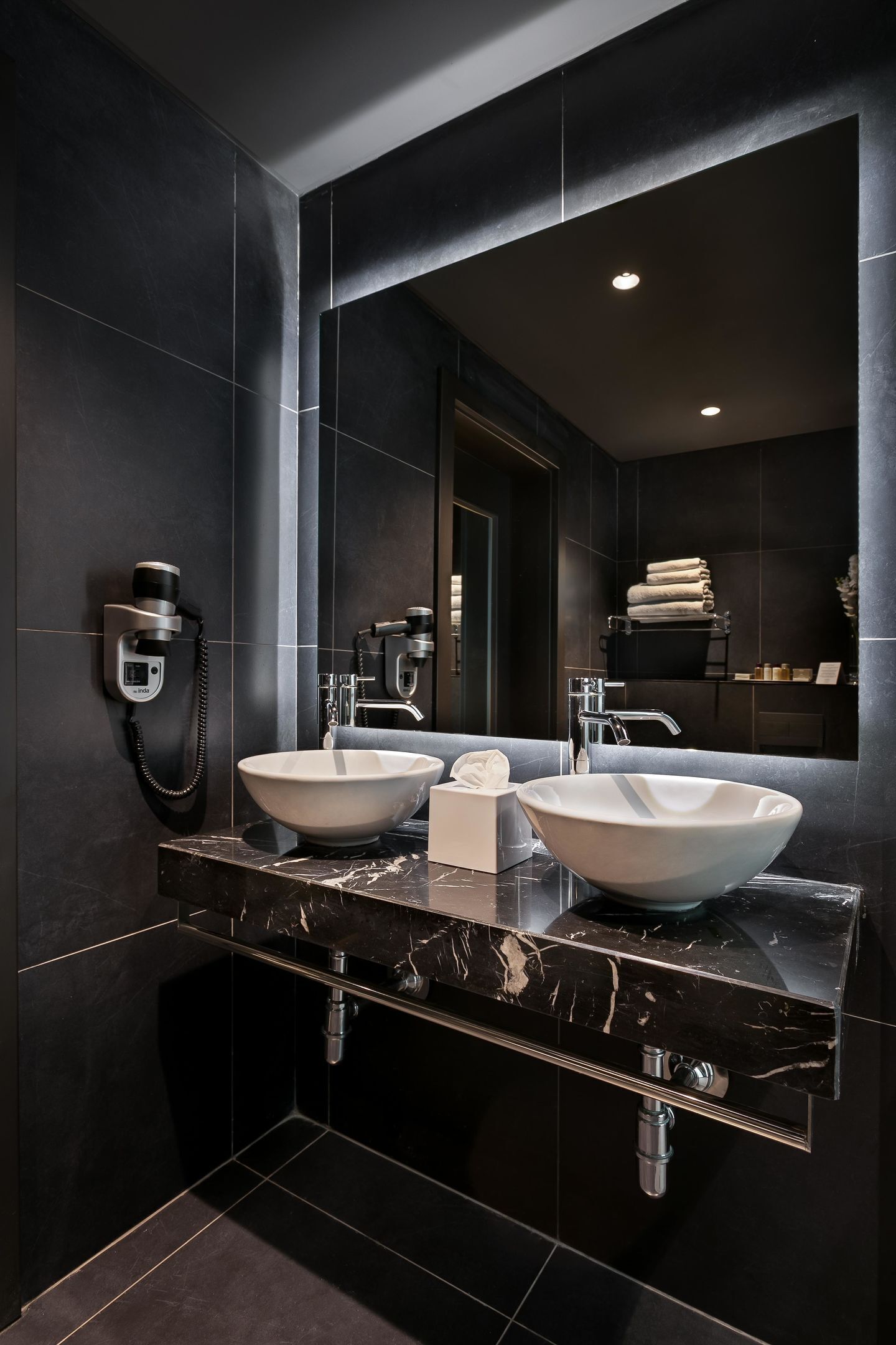 A modern bathroom with two sinks, a large mirror, and a hairdryer mounted on the wall.