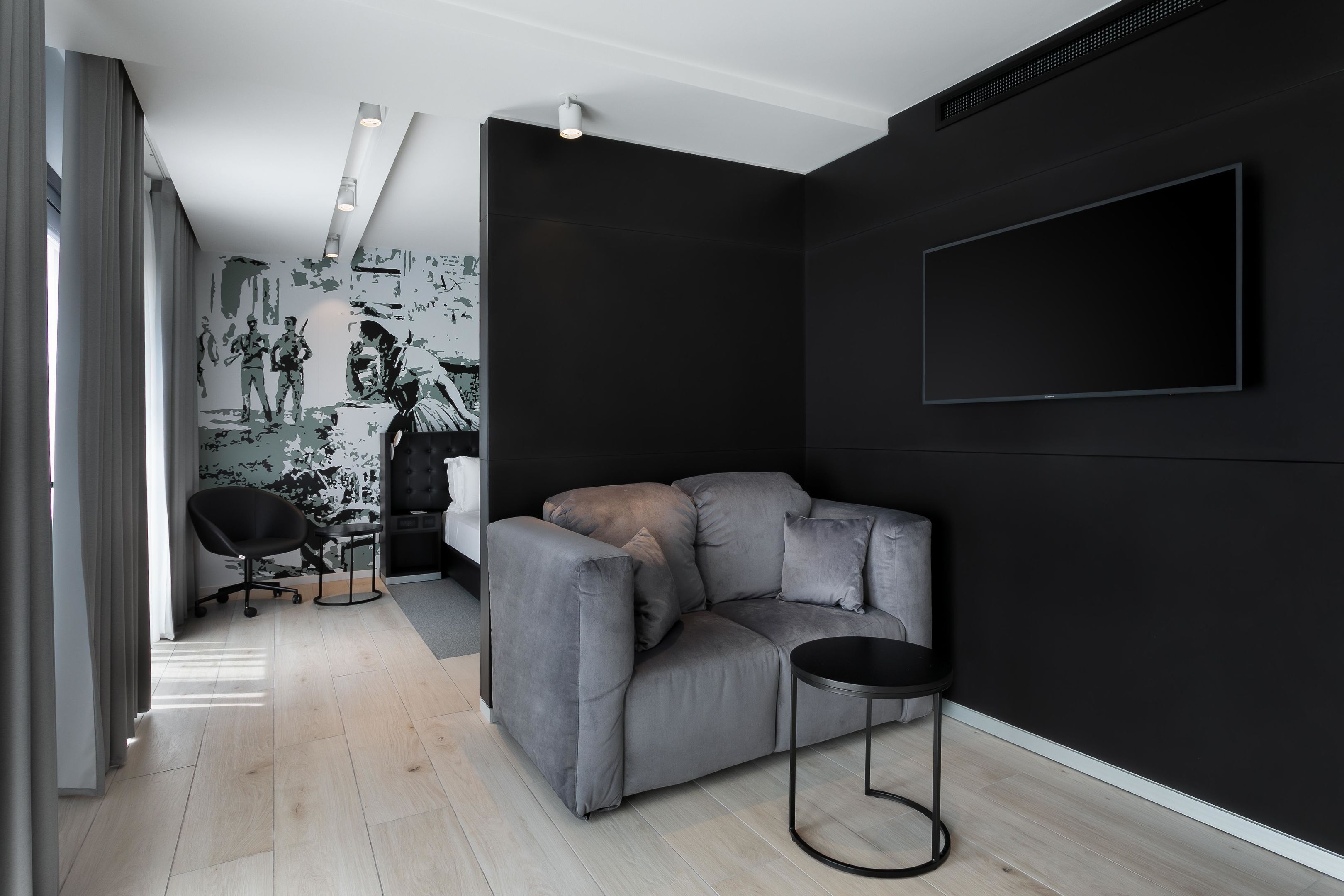 A modern living room with a grey sofa, a black chair, a small round table, and a black wall-mounted TV.