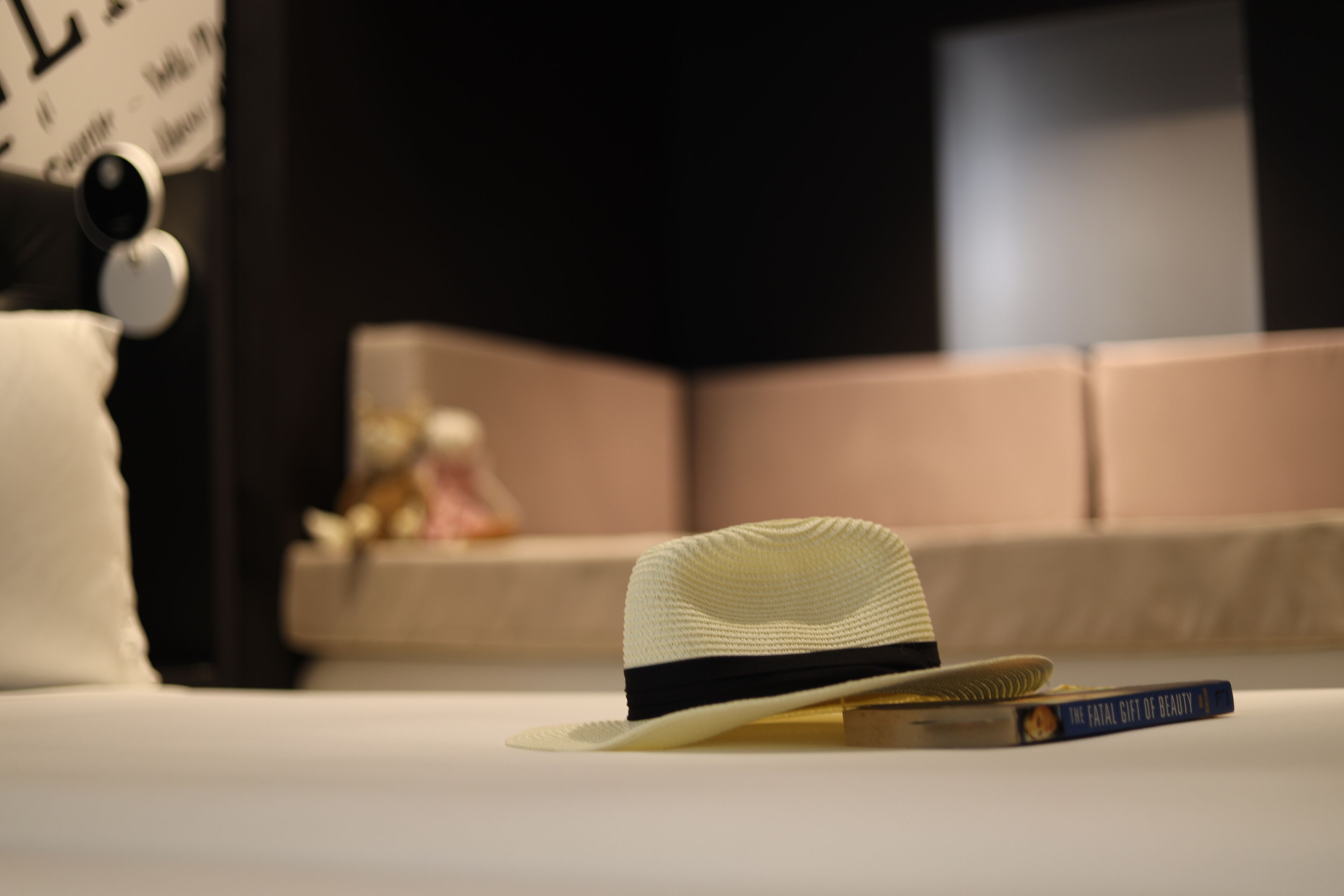 A bed with a white hat and a book titled "The Fatal Gift of Beauty" on it.