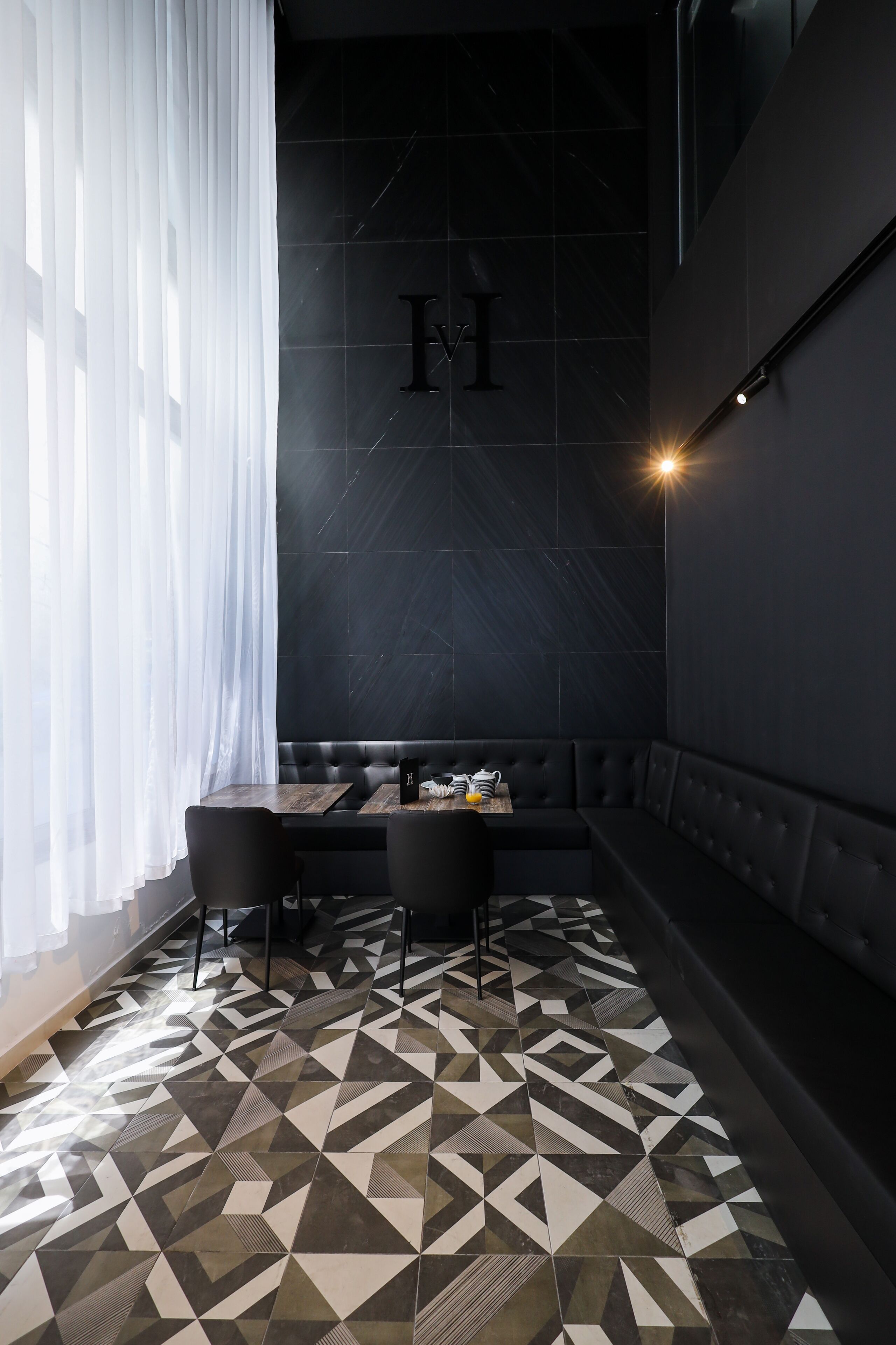 A modern interior with a geometric patterned floor, a dark wall with a logo, and a seating area with a table and chairs.