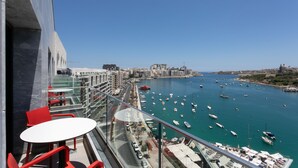Un balcón con sillas rojas y una mesa, con vistas a un puerto deportivo con barcos y edificios al fondo.