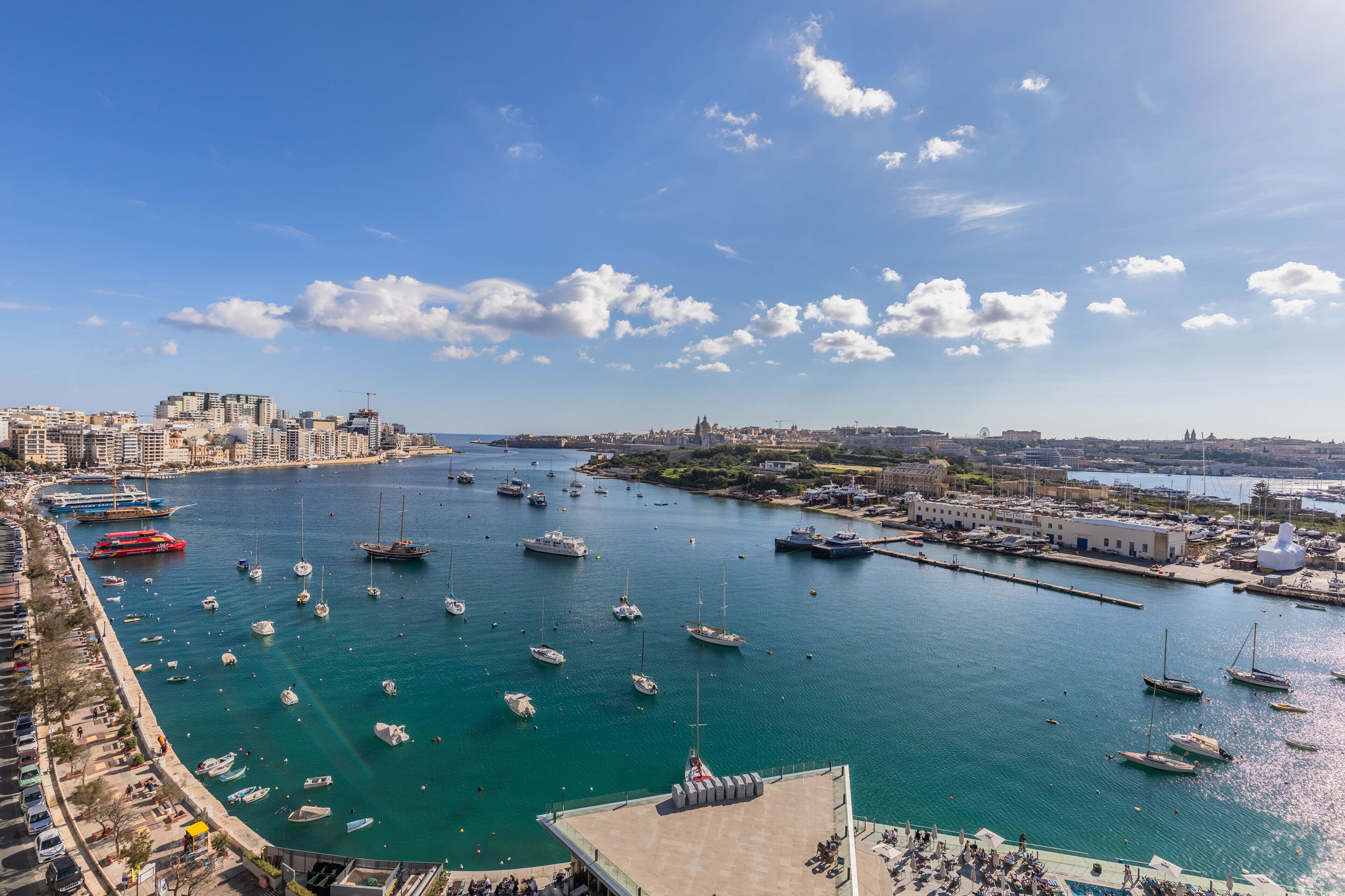 Un port de plaisance où sont amarrés de nombreux bateaux, un paysage urbain côtier en arrière-plan et un ciel dégagé.