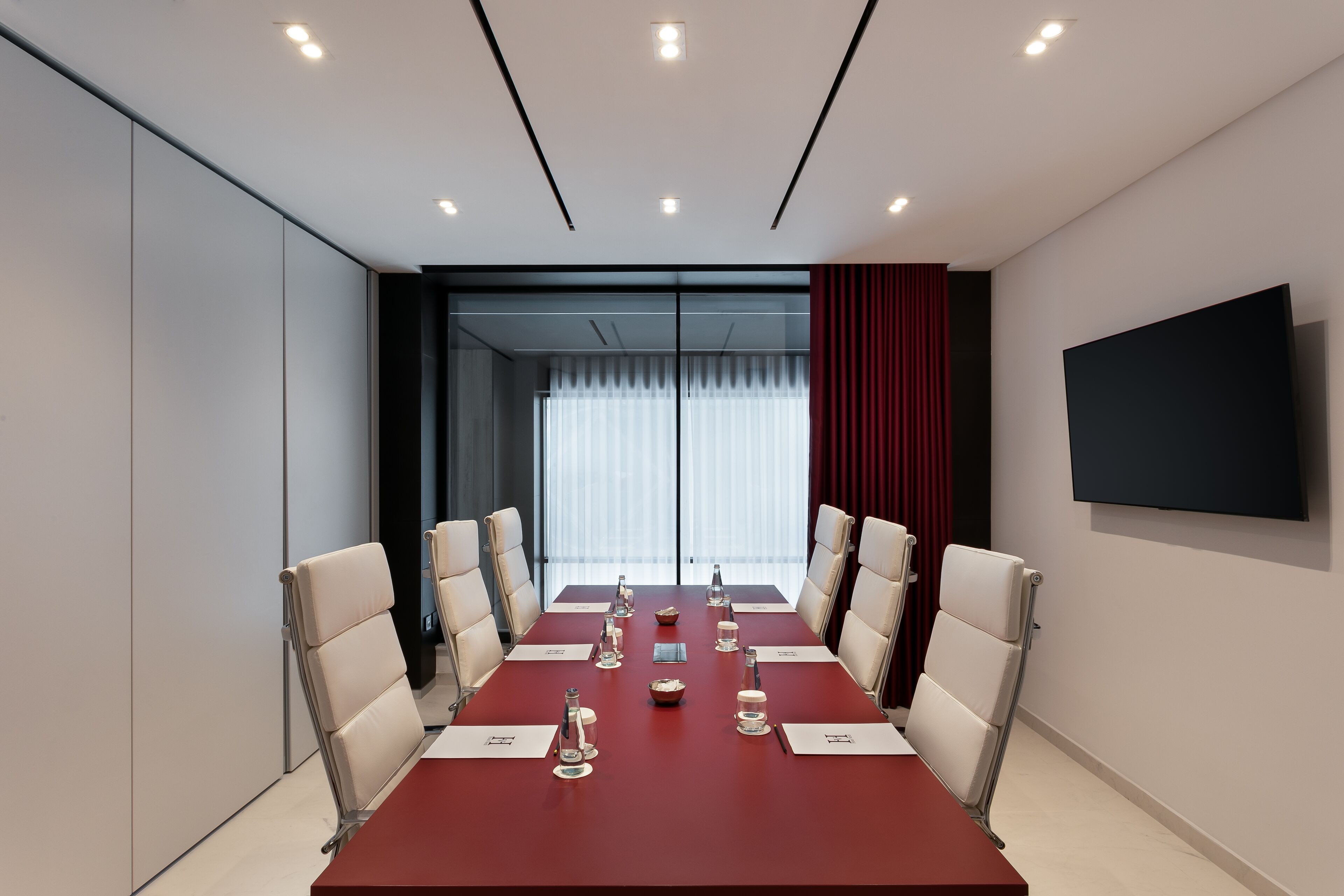 Una sala conferenze con un lungo tavolo, sedie e un televisore appeso al muro.
