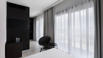 Una habitación de hotel moderna con una cama grande, un escritorio negro, una silla y un televisor montado en la pared.