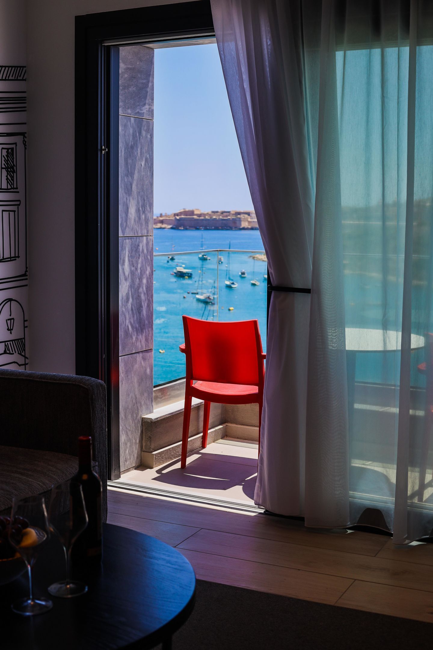 Una habitación con vista al mar, una silla roja y una mesa con una botella y un vaso.