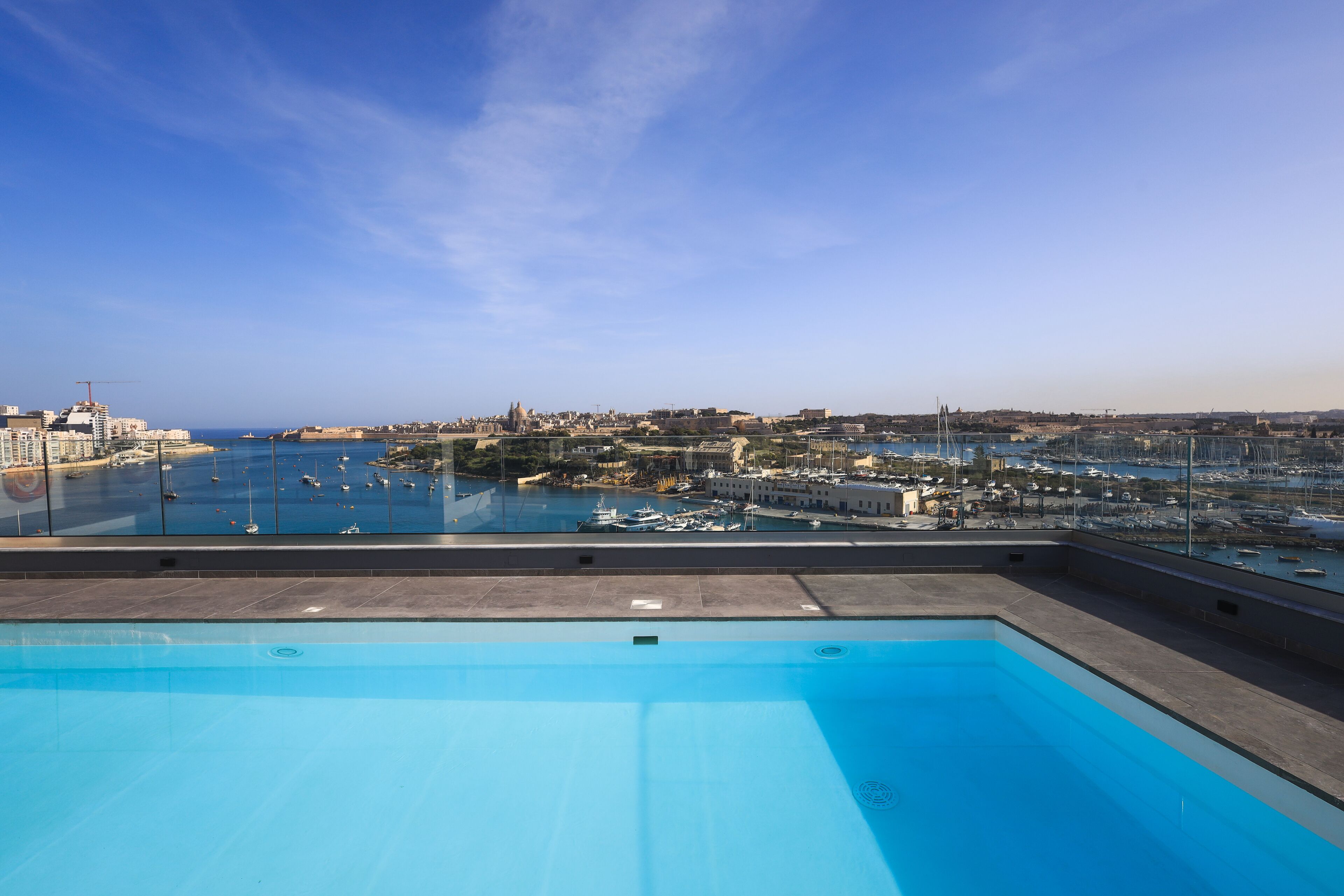 A rooftop pool with a view of a marina and cityscape.