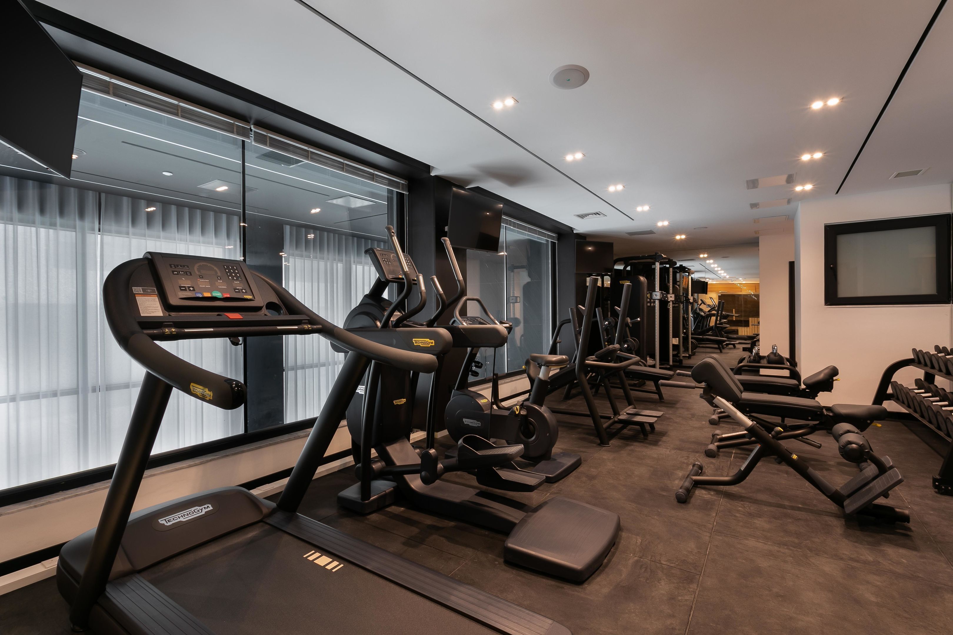 Ein Fitnessstudio mit Laufbändern, Kraftgeräten und einem großen Fenster.