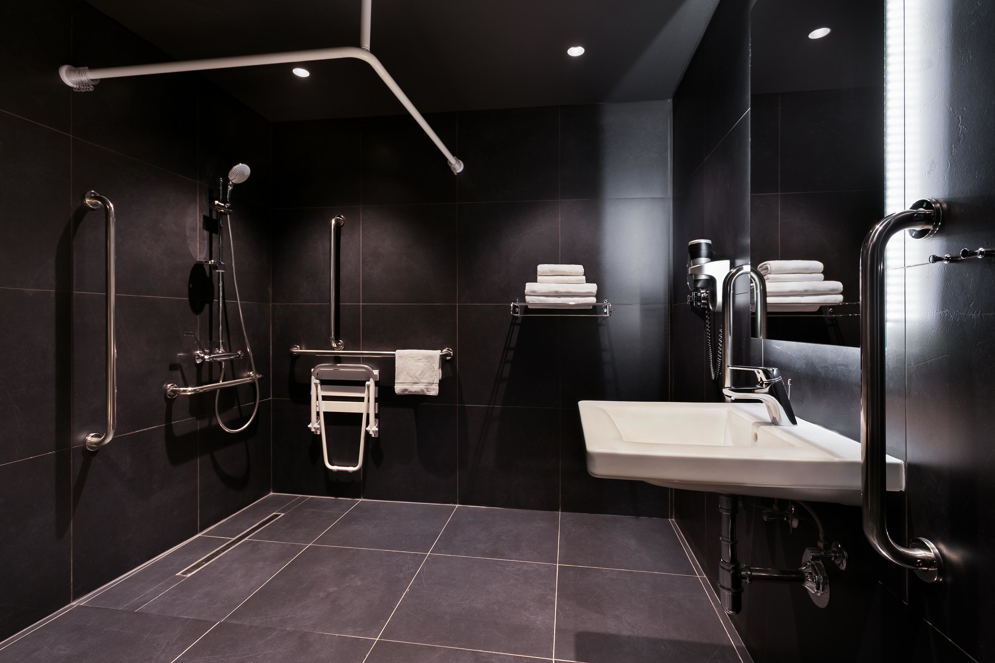 A modern bathroom with a walk-in shower, grab bars, a sink, and a towel rack.