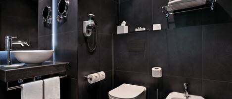 A modern bathroom with a large sink, toilet, bidet, and a towel rack.