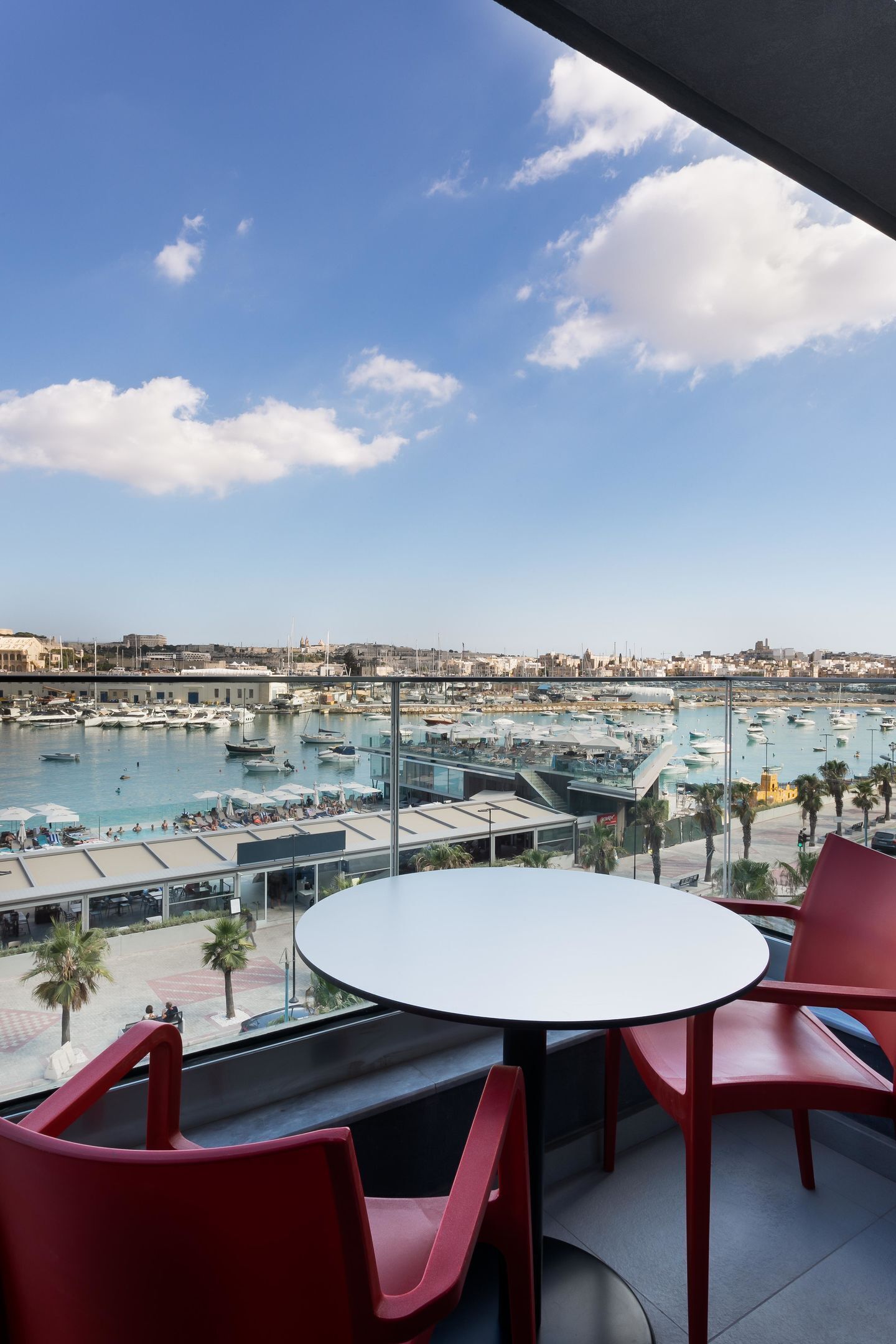 A balcony with a table and chairs, overlooking a marina with boats and a cityscape.