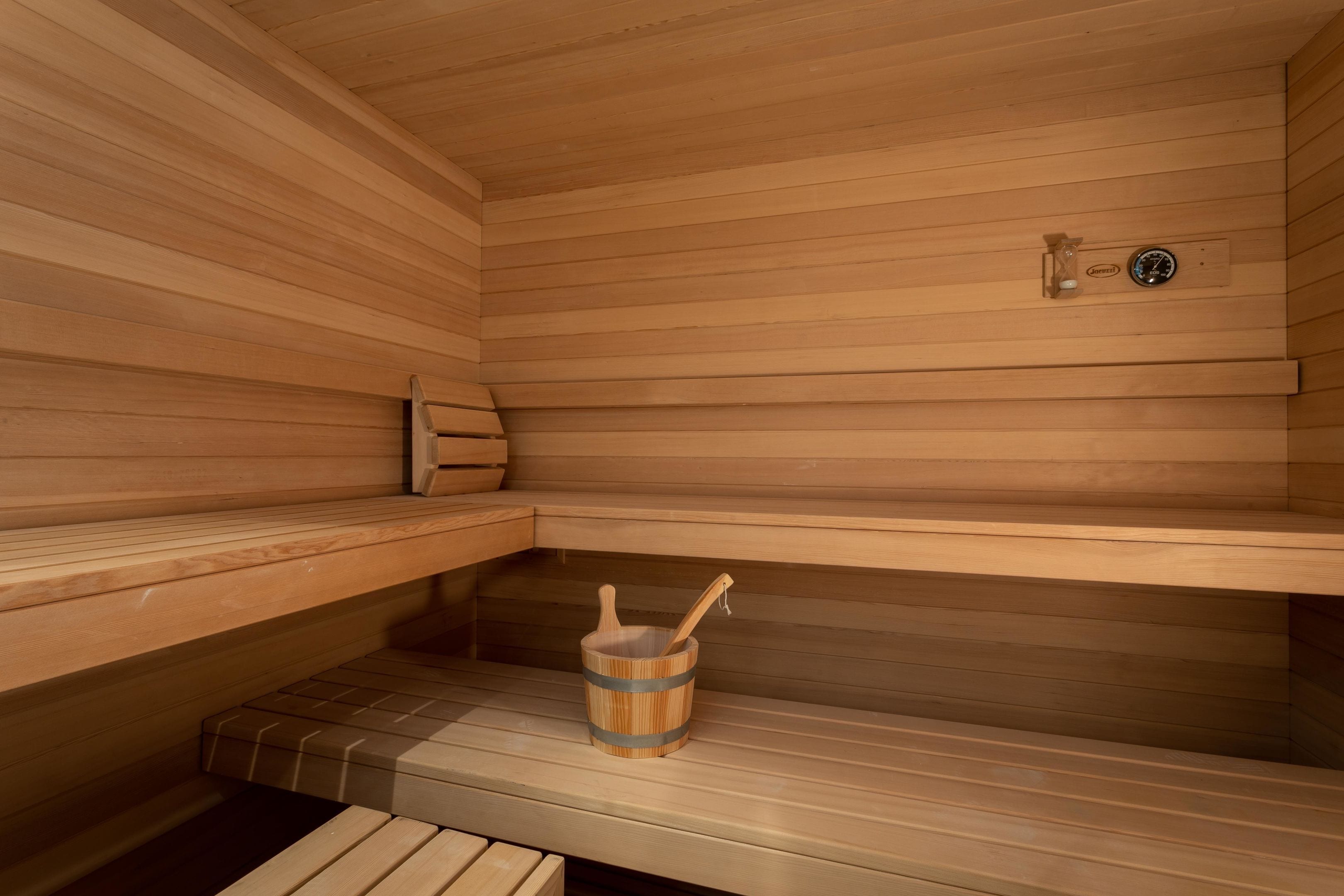 A sauna with wooden benches, a wooden bucket with a brush, and a control panel.