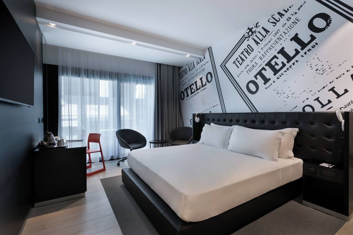 A modern hotel room with a large bed, a desk with a chair, and a television.