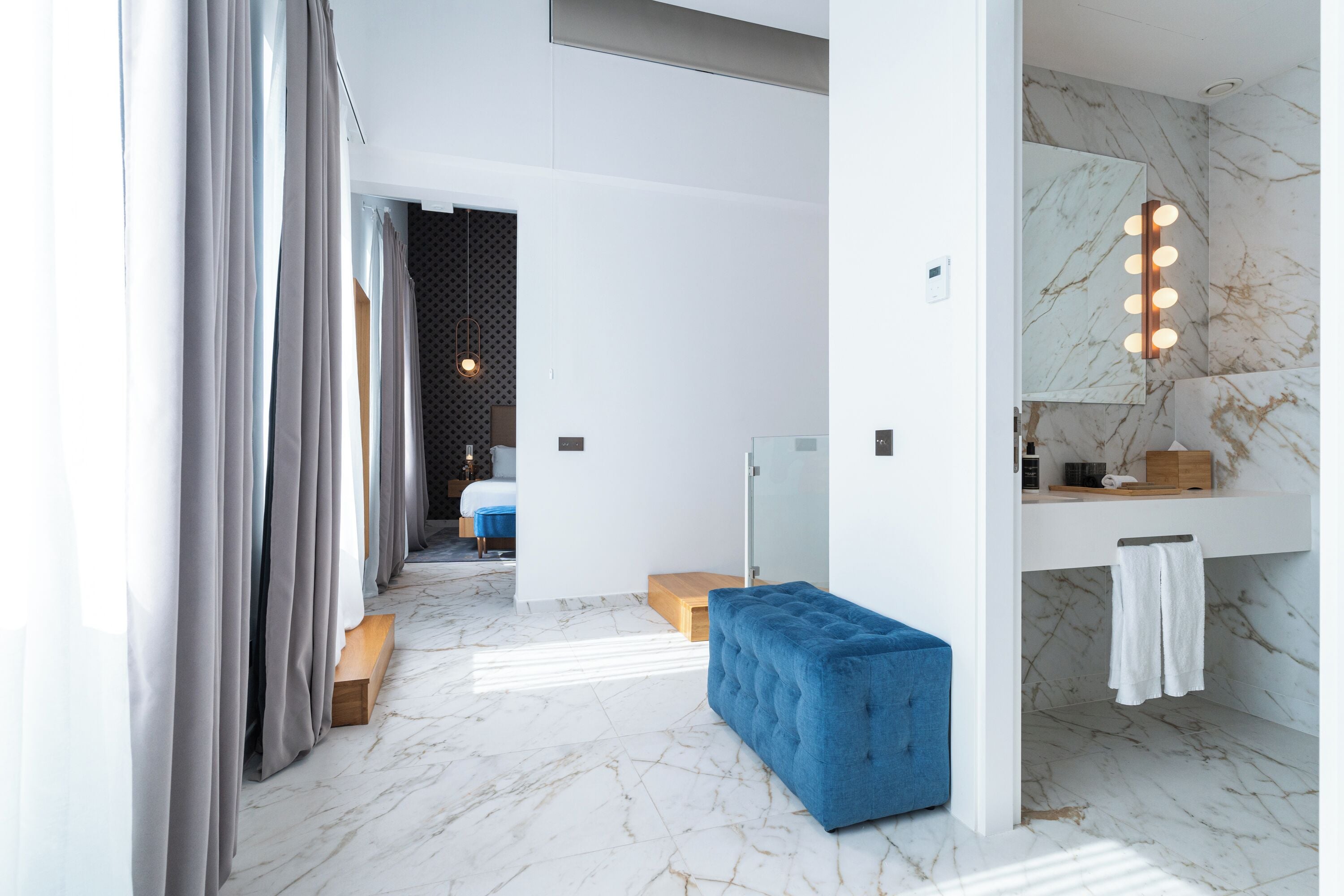 A modern bathroom with a marble floor, a blue bench, a mirror with lights, and a towel rack.