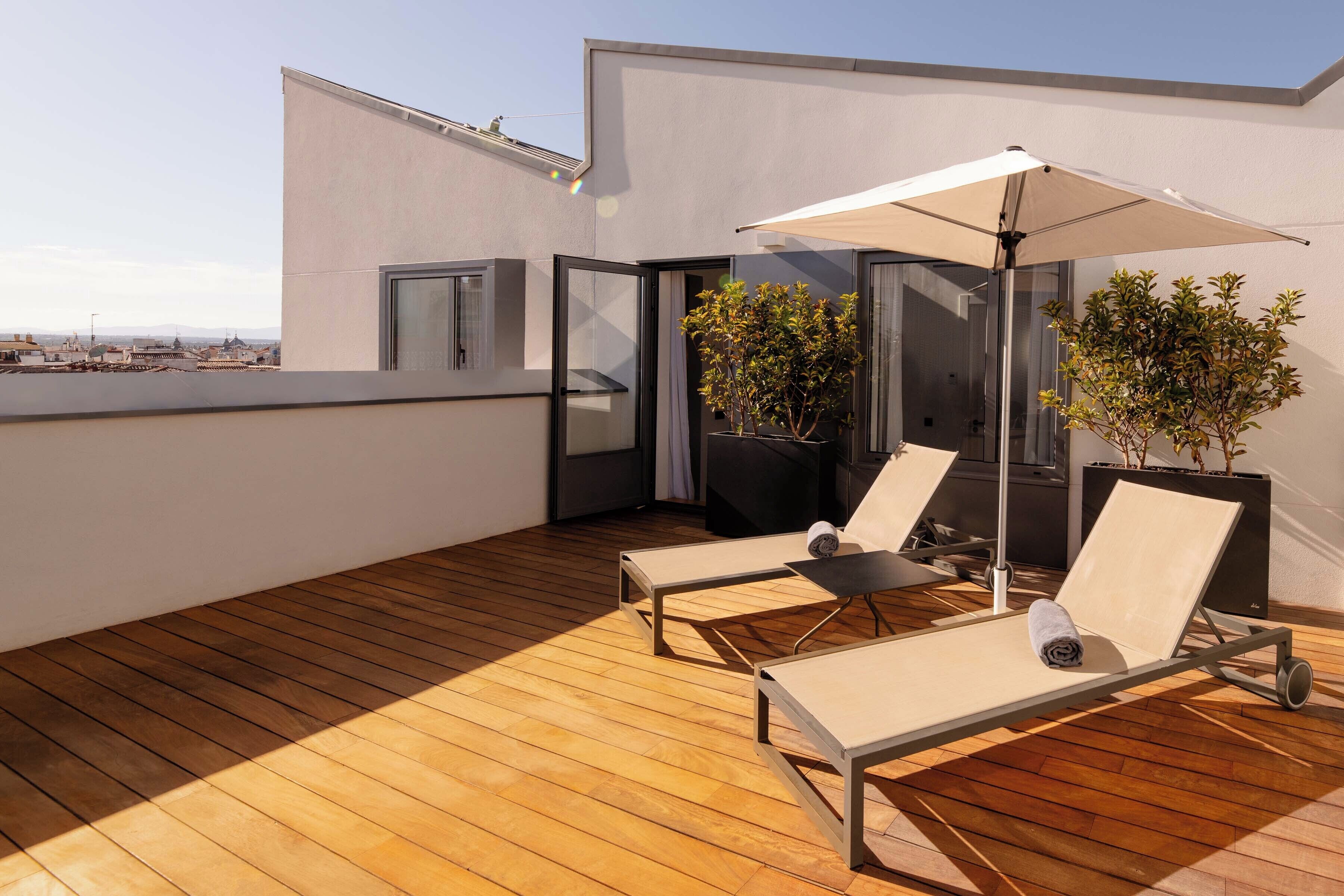 Una terraza en la azotea con suelo de madera, dos sillones de relax con dosel y plantas en macetas.