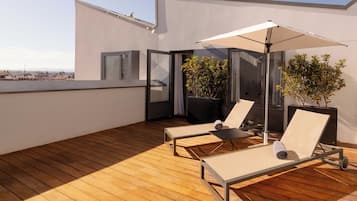 Una terraza en la azotea con suelo de madera, dos sillones de relax con dosel y plantas en macetas.