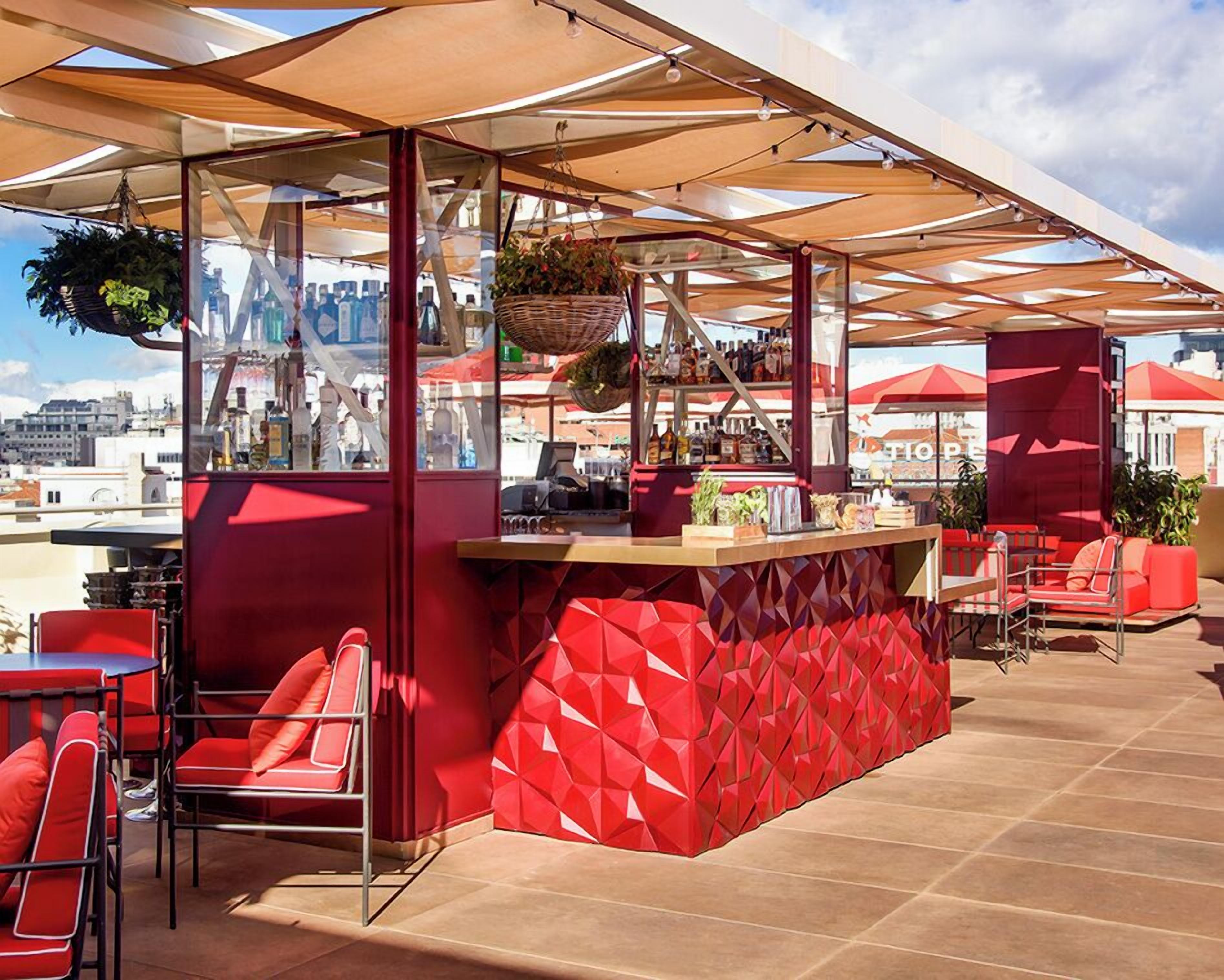 An outdoor bar area with red seating and a counter displaying various bottles.