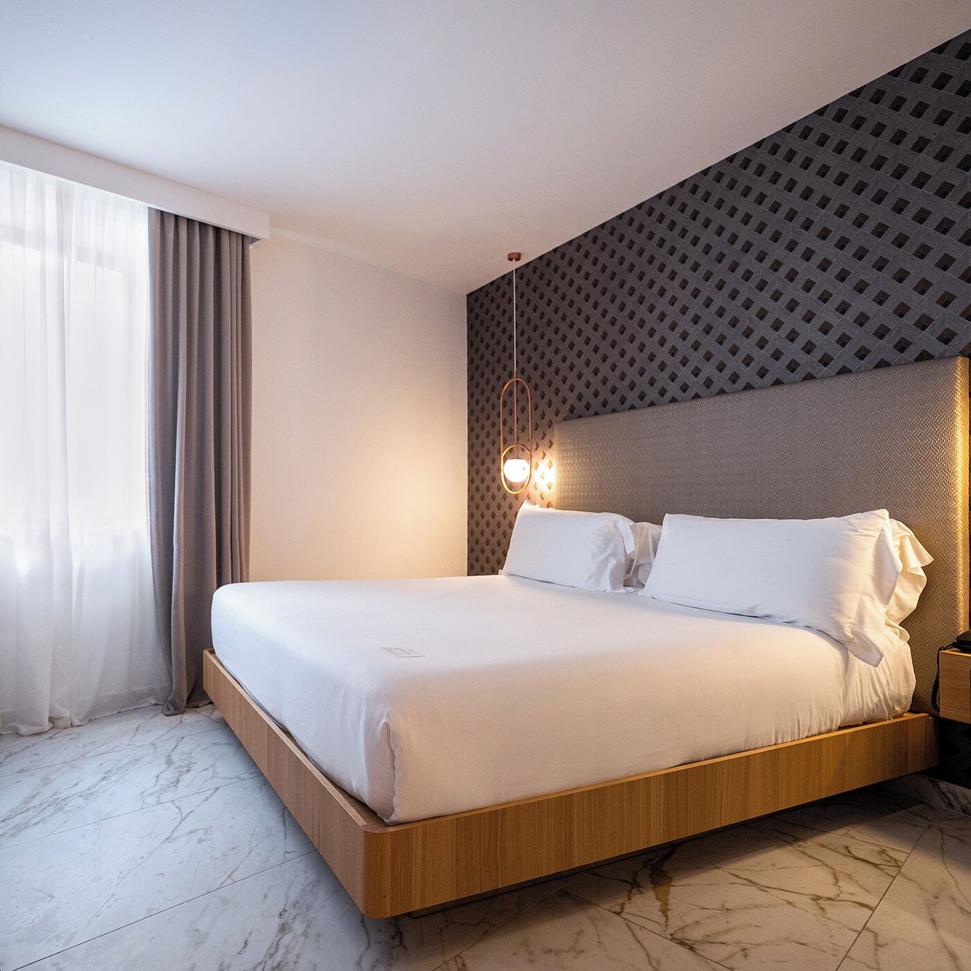 Habitación de hotel moderna con una cama grande, cabecero de madera y una pared decorativa con estampado.