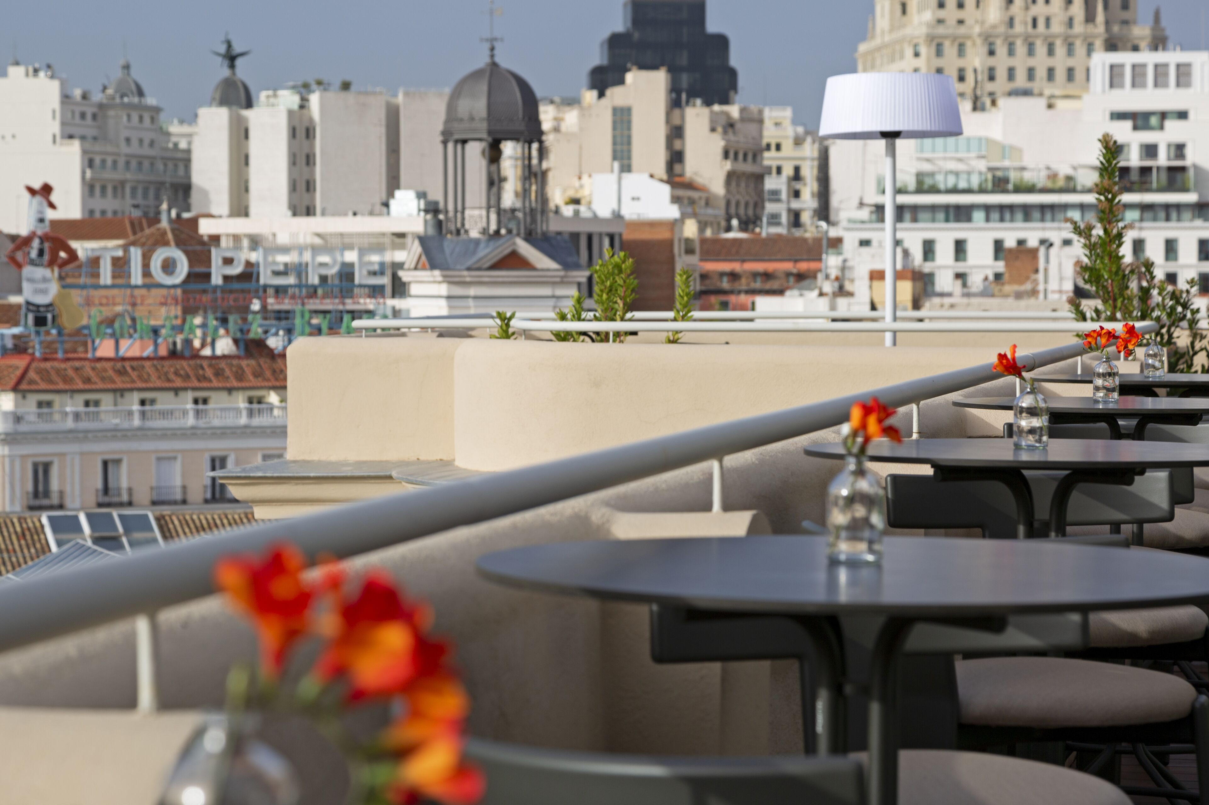 A rooftop terrace with tables and chairs, a cityscape view, and a decorative sculpture.
