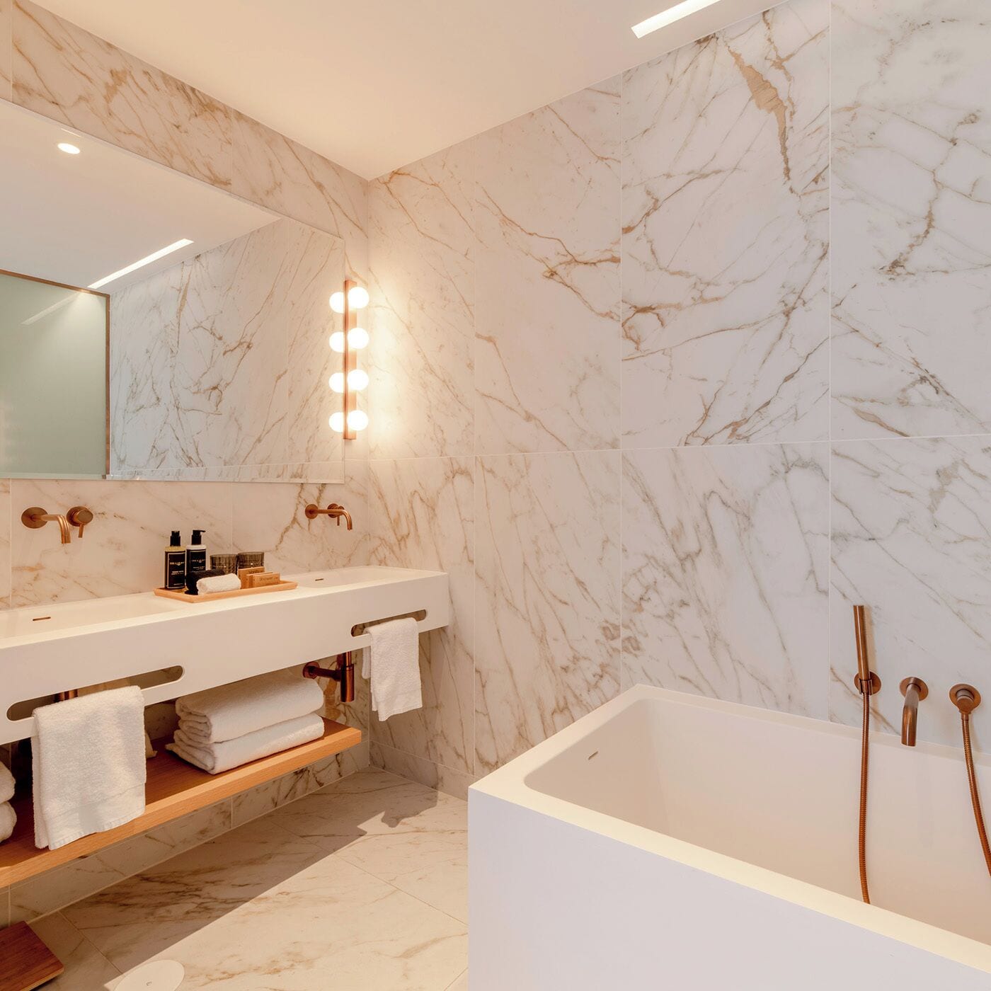 A modern bathroom with marble walls, a vanity with a mirror, and a bathtub.