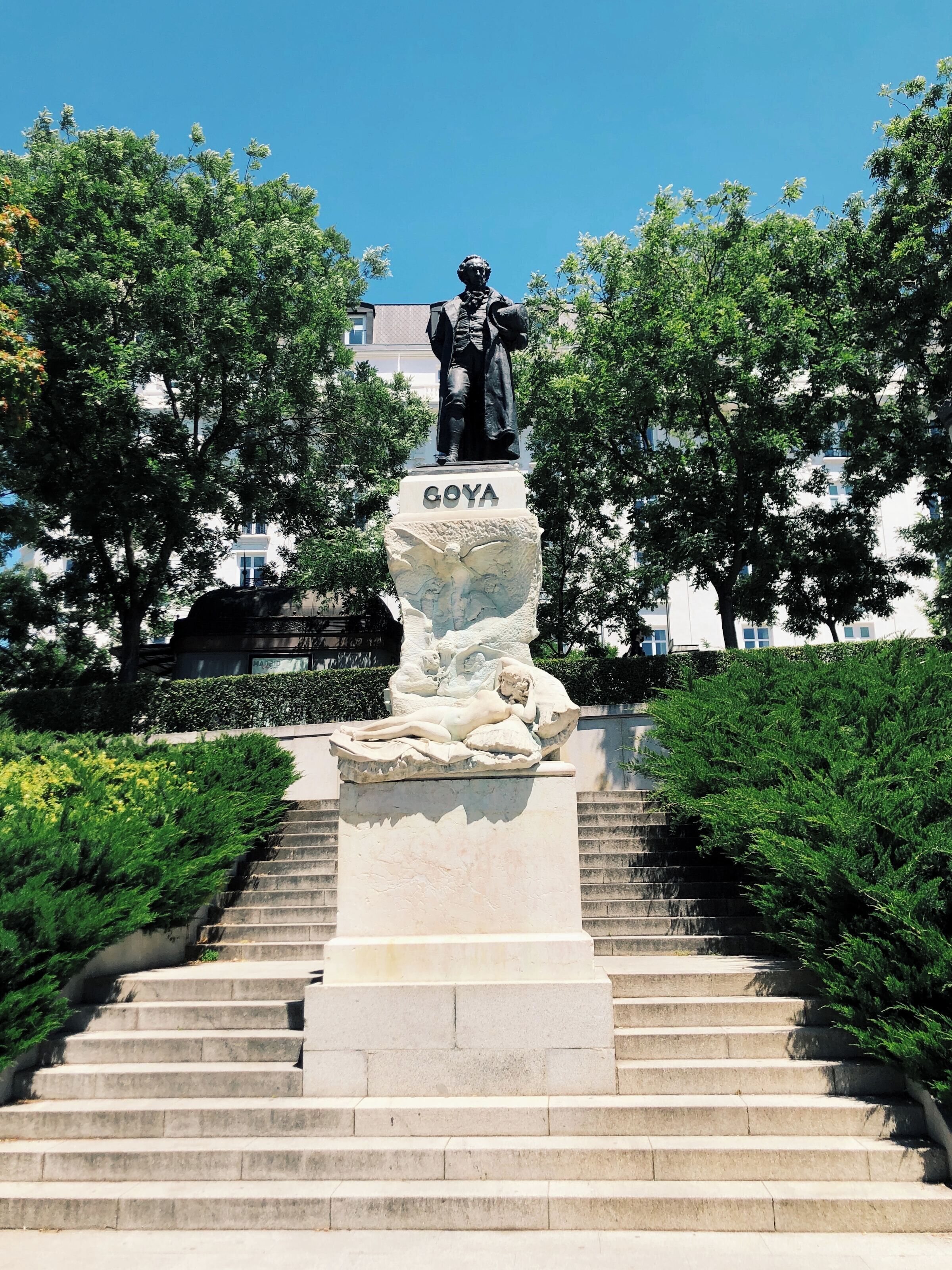 Estàtua d'un home sobre un pedestal amb el nom 'GOYA', envoltada d'escales i vegetació.