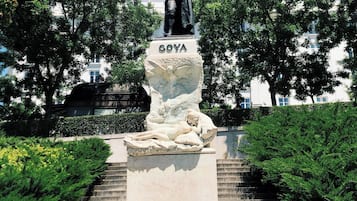 Estàtua d'un home sobre un pedestal amb el nom 'GOYA', envoltada d'escales i vegetació.