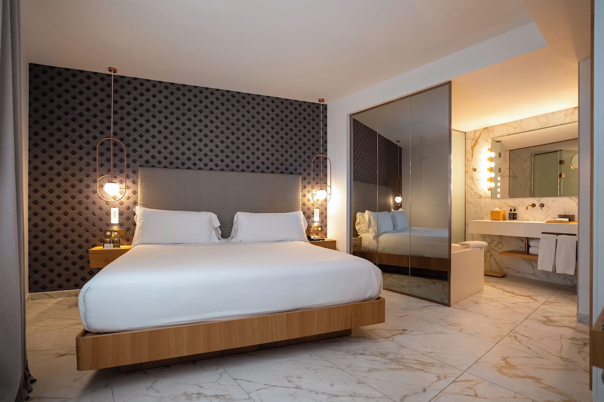A modern hotel room with a large bed, a vanity with a mirror, and a bathroom.