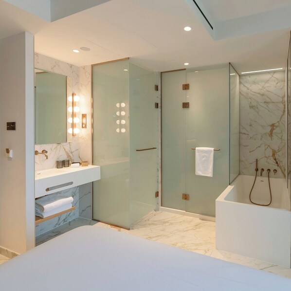 A modern bathroom with a glass-enclosed shower, a vanity with a marble countertop, and a large mirror with lights. - UMusic Hotel Madrid (Madrid)