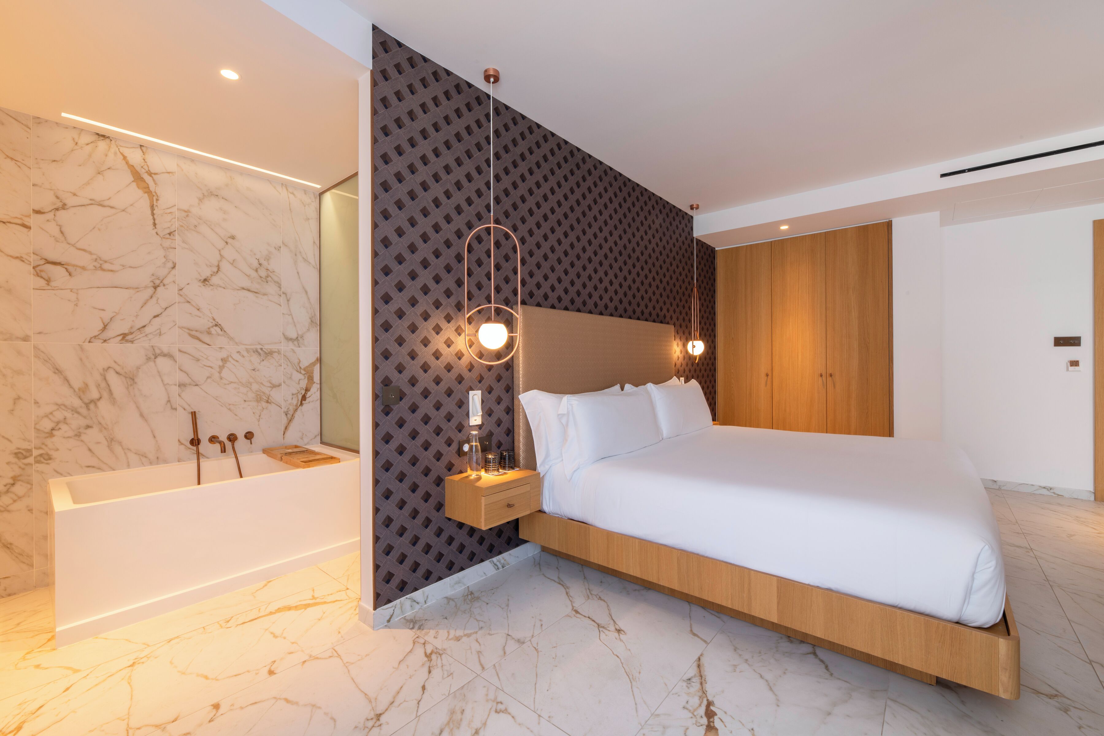 Un dormitorio moderno con una cama grande, cabecera de madera, mesita de noche con lámpara y suelo de baldosas de mármol.
