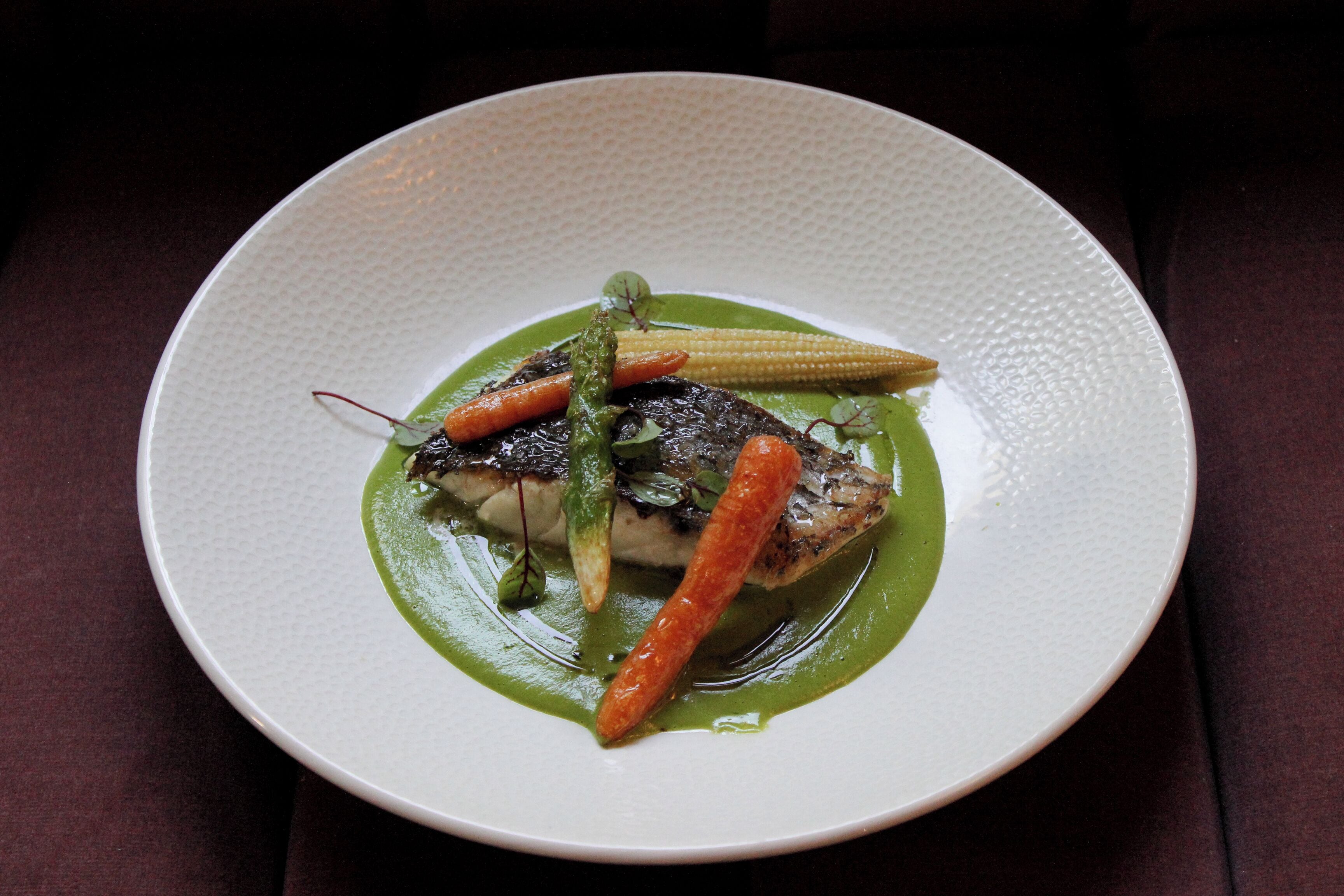 Un piatto bianco con un piatto di pesce, verdure e salsa verde.