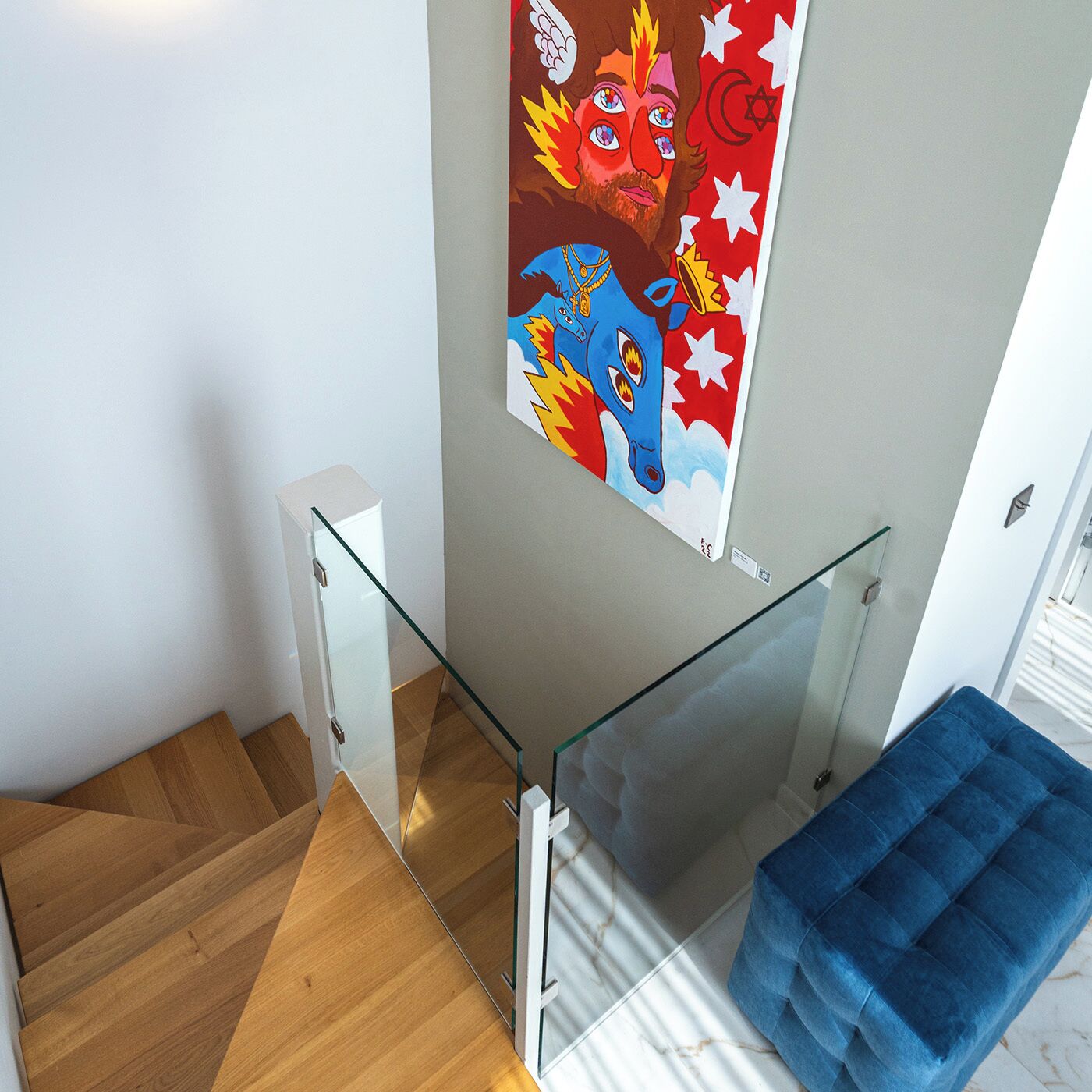 A modern staircase with glass railings, a blue cushioned bench, and a colorful wall art piece.