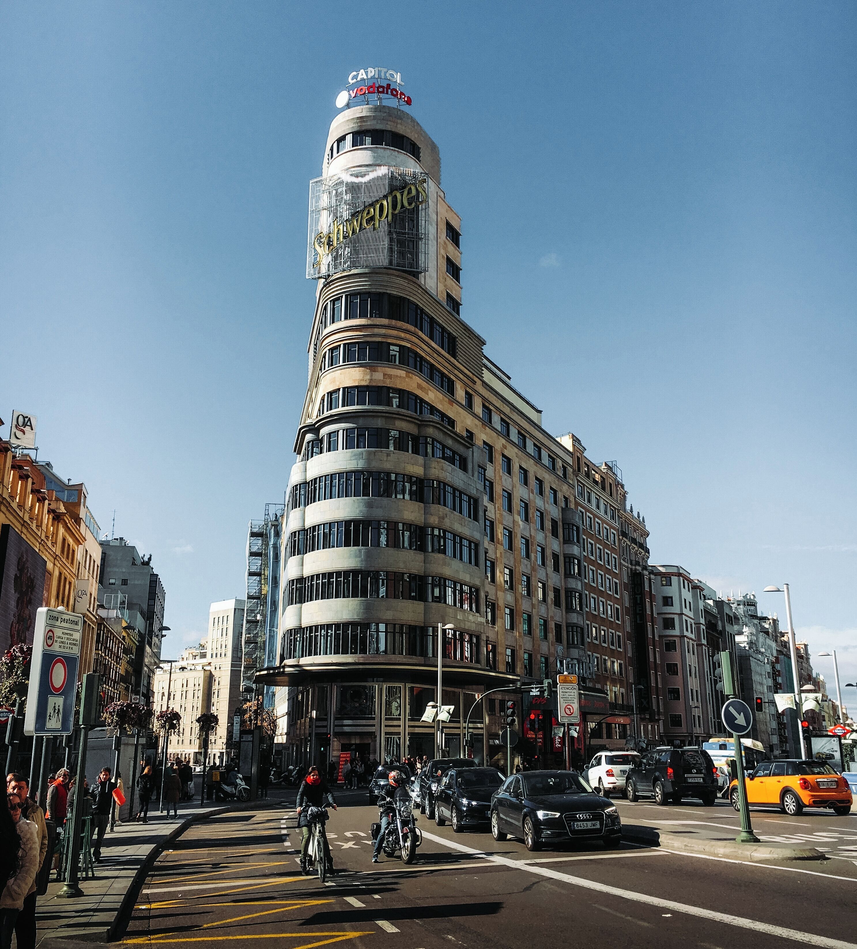 Un immeuble à plusieurs étages doté d’une façade incurvée, d’une enseigne bien visible au sommet et situé sur une rue animée.