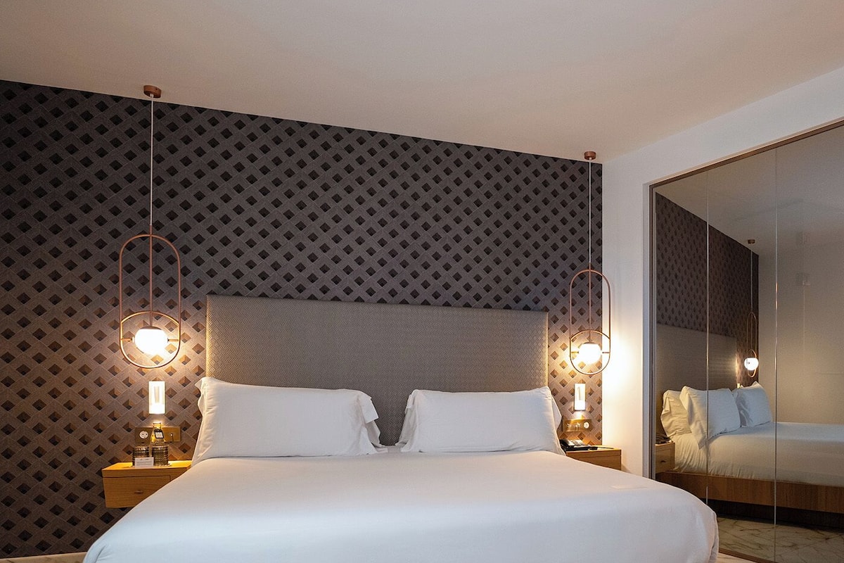 A modern hotel room with a large bed, wooden headboard, and a patterned wall.