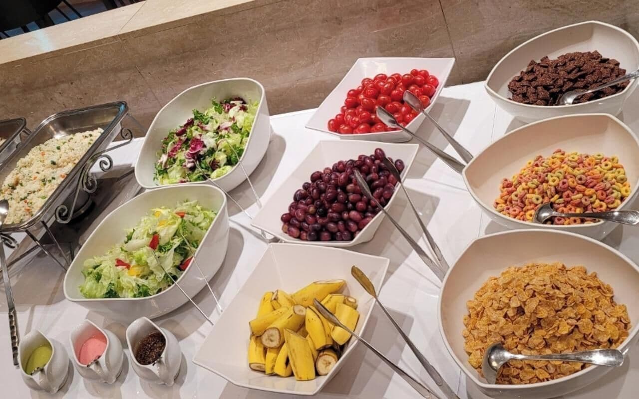 Una mesa de buffet con diversos alimentos, como ensaladas, frutas y cereales.