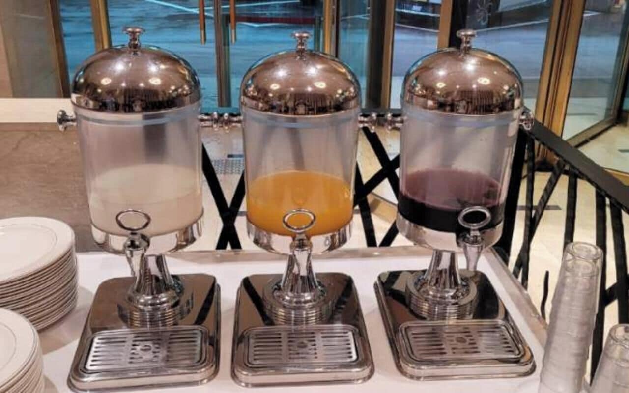A beverage dispenser station with three transparent containers, each with a metallic lid and pump.