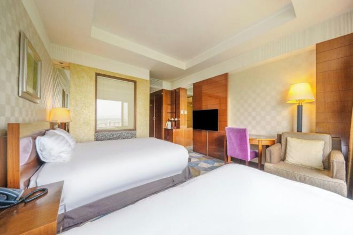 Ein Hotelzimmer mit zwei Betten, einem Fernseher, einem Schreibtisch mit Lampe und einem Sofa.