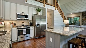 Una cocina moderna con armarios blancos, electrodomésticos de acero inoxidable, piso de madera y chimenea de piedra.
