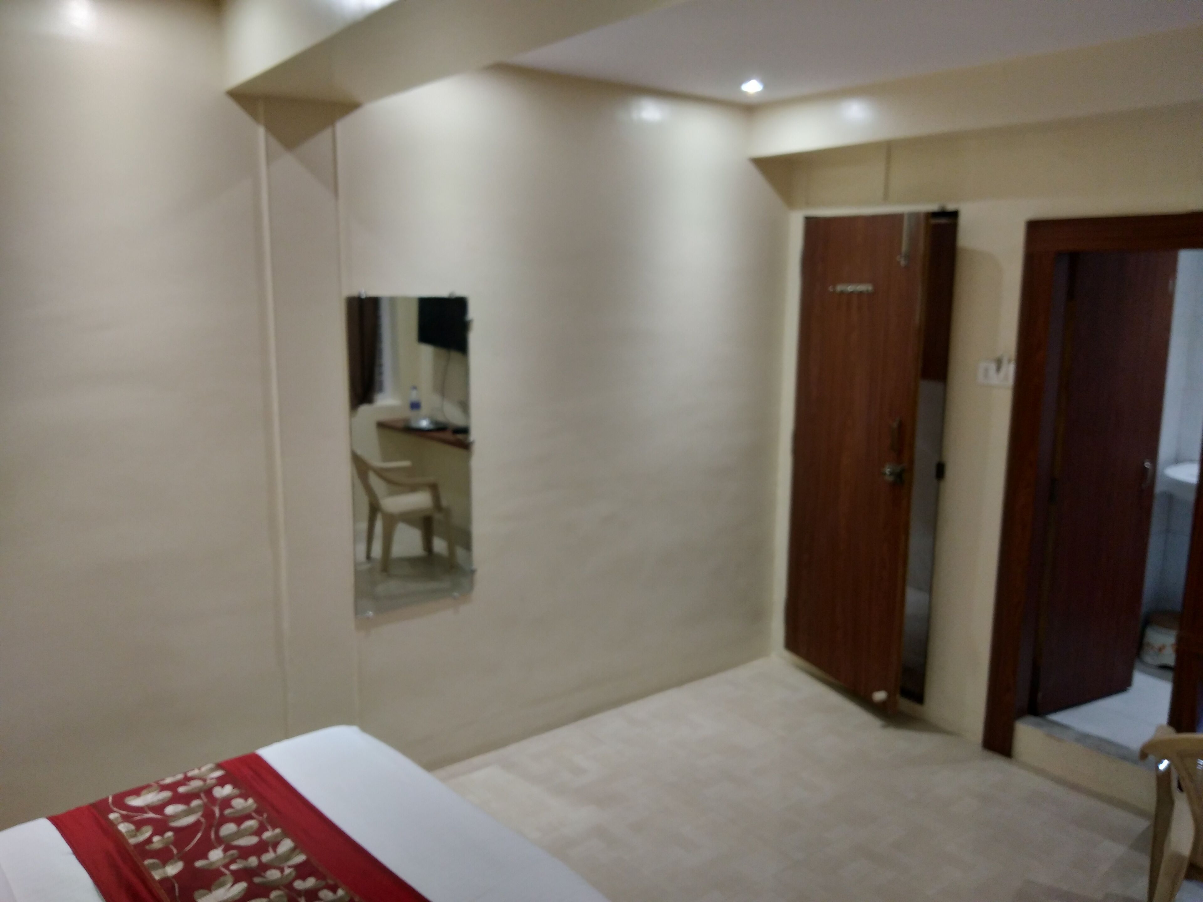 Une chambre avec un lit, un bureau et une chaise. Il y a une porte et un miroir sur le mur.