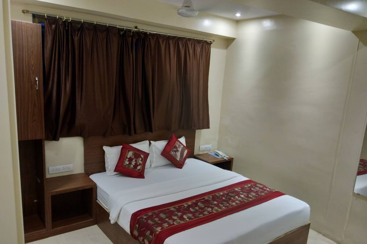 A neatly made bed with white linens and red accents, a wooden headboard, and a bedside table with a phone and a lamp.