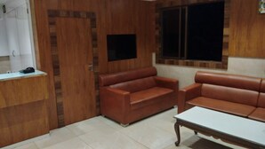 Una habitación con una pared de madera decorativa, un televisor de pantalla plana montado en ella, dos sofás de cuero marrón, una mesa de centro blanca y un piso cubierto de baldosas.