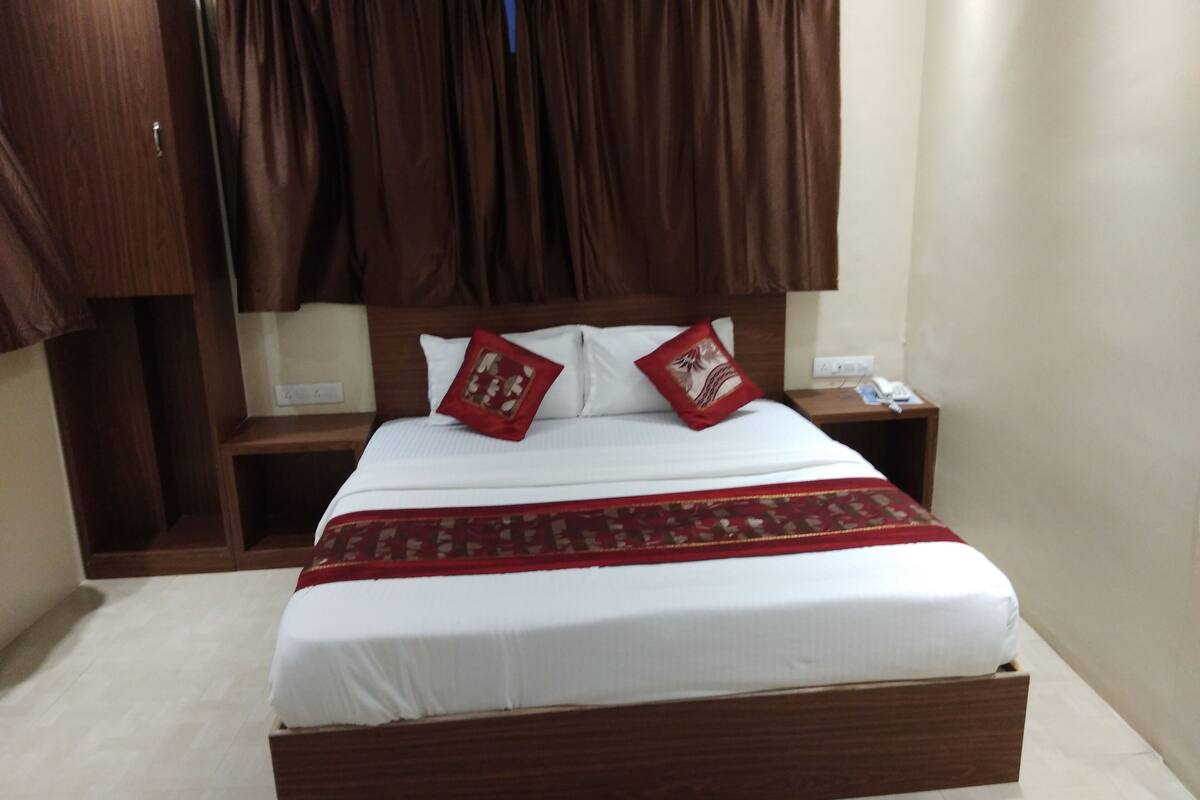 A neatly made bed with a wooden frame, two pillows, and a red decorative pillow.