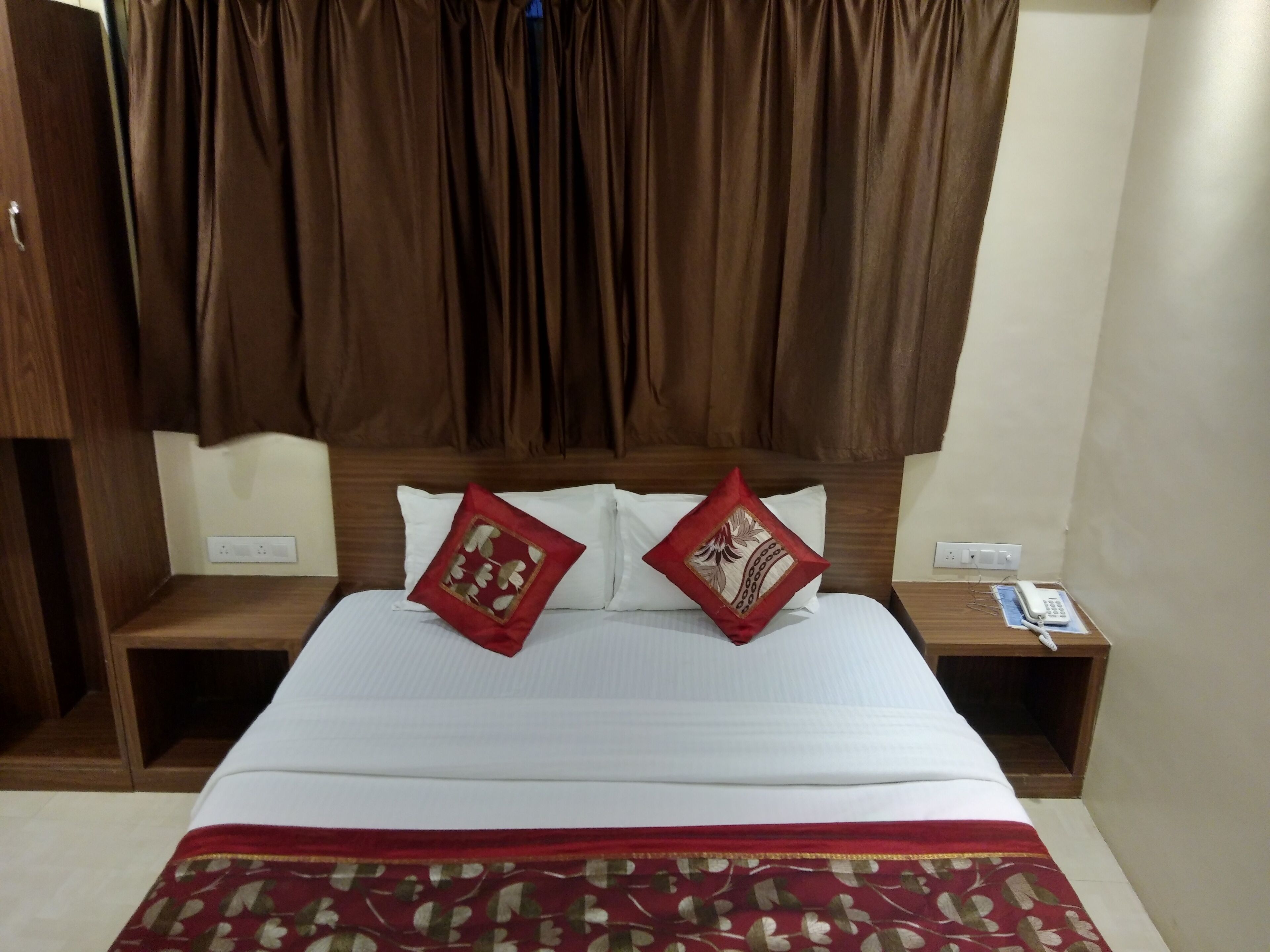 A hotel room with a bed, two pillows, a bedside table with a phone, and a wooden headboard.