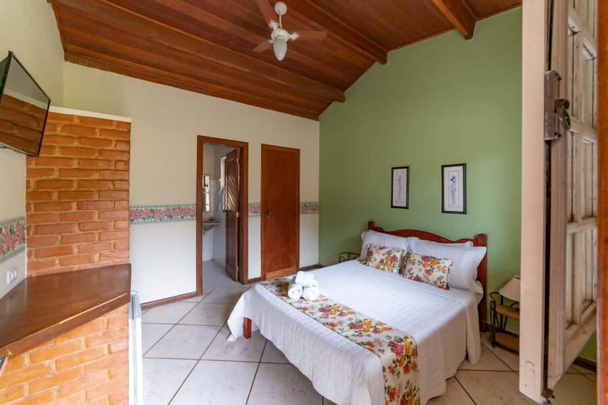 A bedroom with a bed, a wooden ceiling, a brick wall, and a door leading to another room.