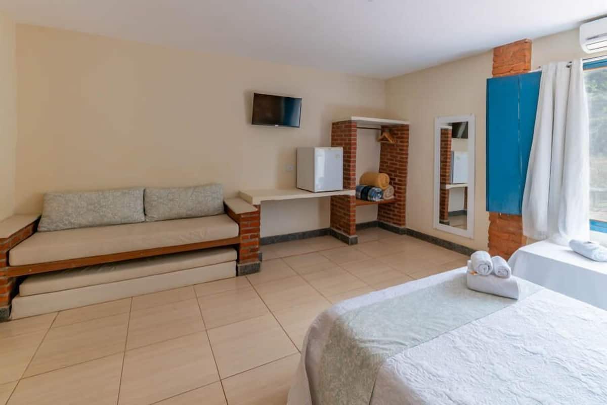 A hotel room with a bed, a sofa, a TV, a small table, and a brick wall.